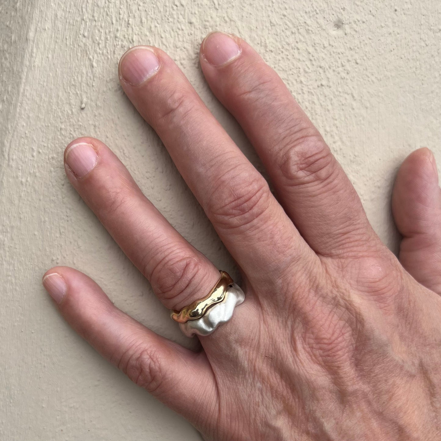 The matt silver wave ring and the 9ct yellow gold bubble ring on a hand with a cream background.