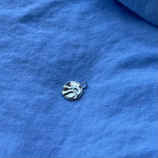 The sterling silver shiny pebble pendant on a blue background.