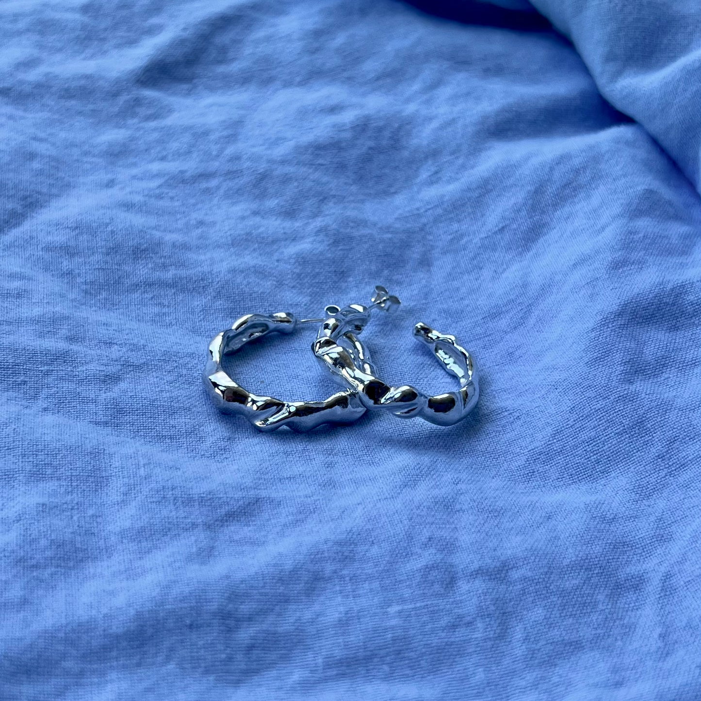 Large wavy sterling silver hoops on a blue linen background.
