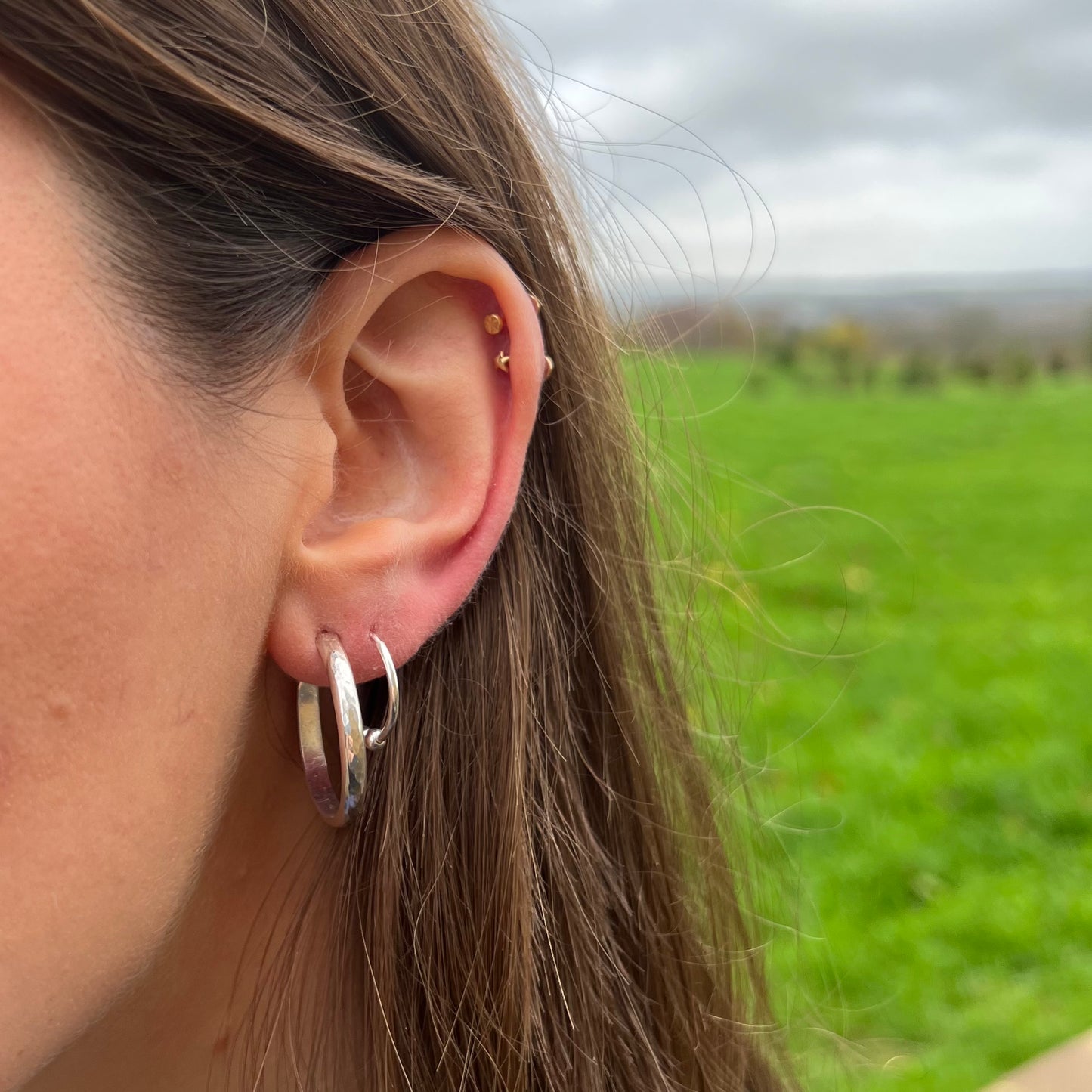 Slim sterling silver hammered hoop earrings, shown on a model.