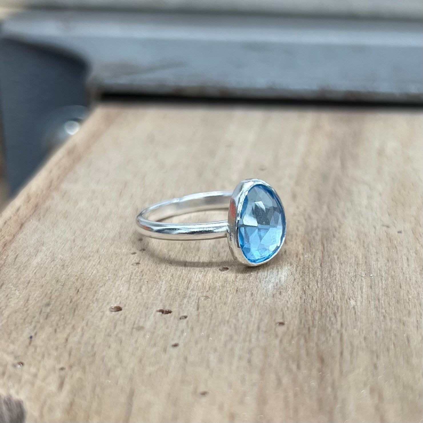 A blue topaz and sterling silver ring on a wooden background.