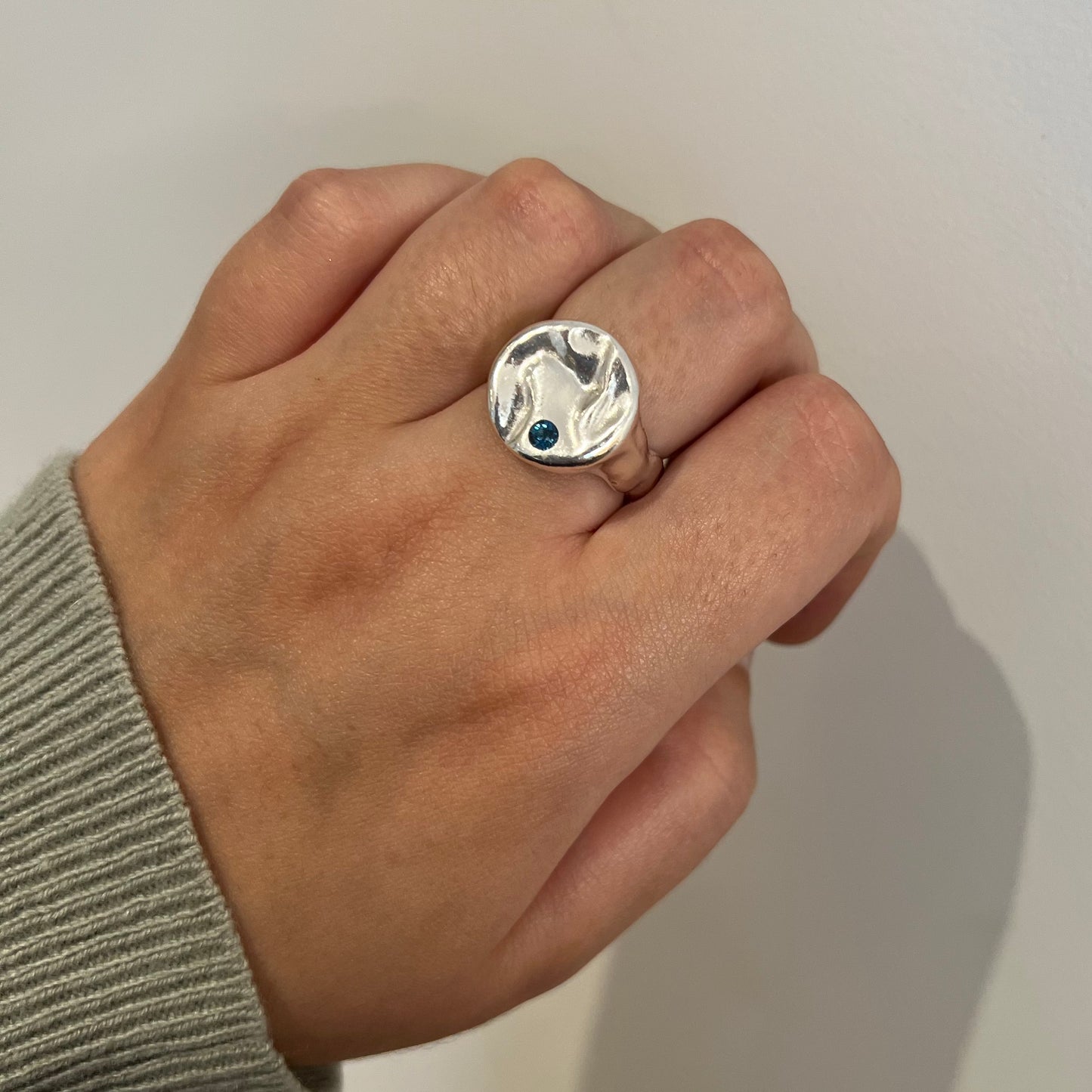 A sterling silver & blue topaz splash ring on a hand with a white background.