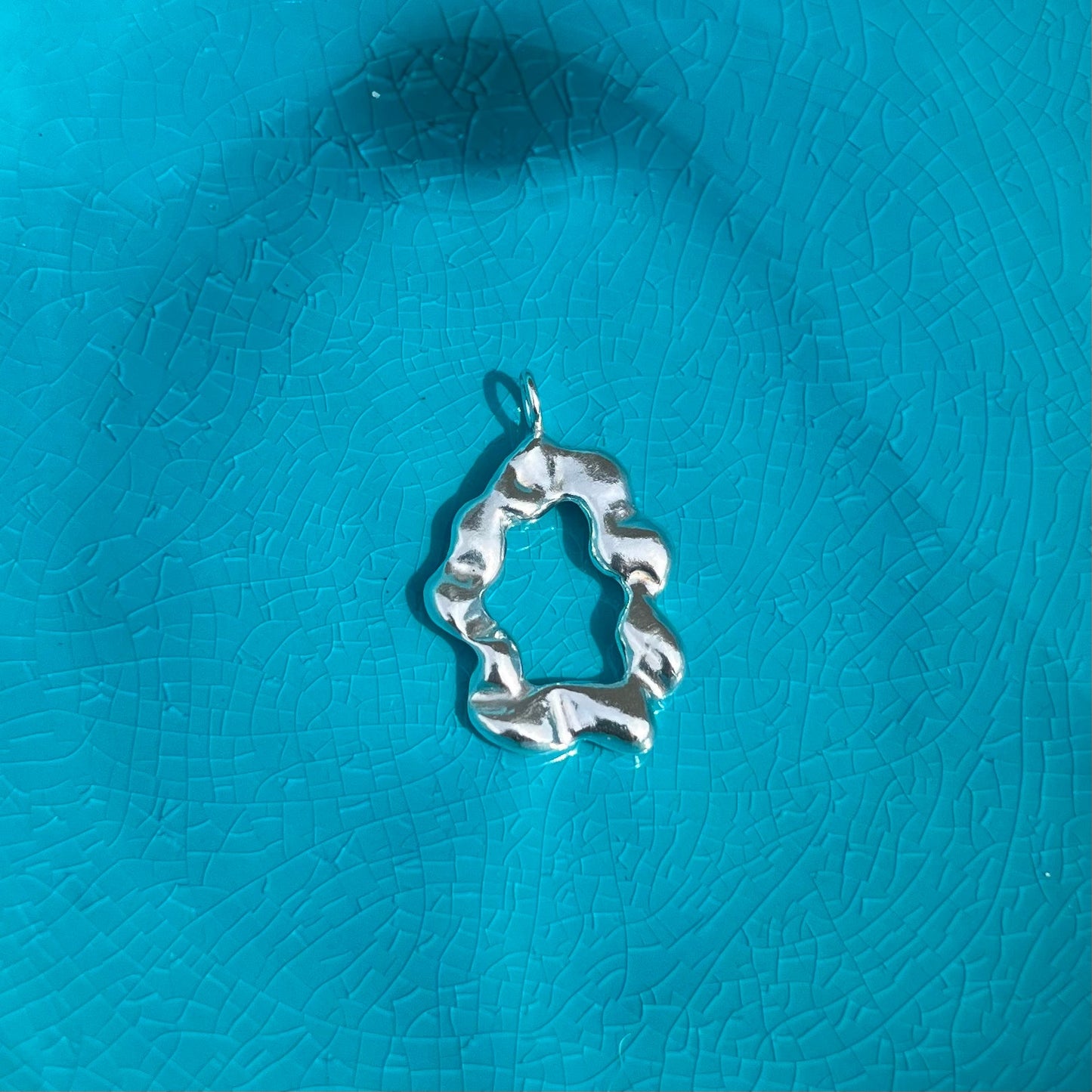 The 'Cloud pendant'. A sterling silver abstract pendant on an azure blue background.