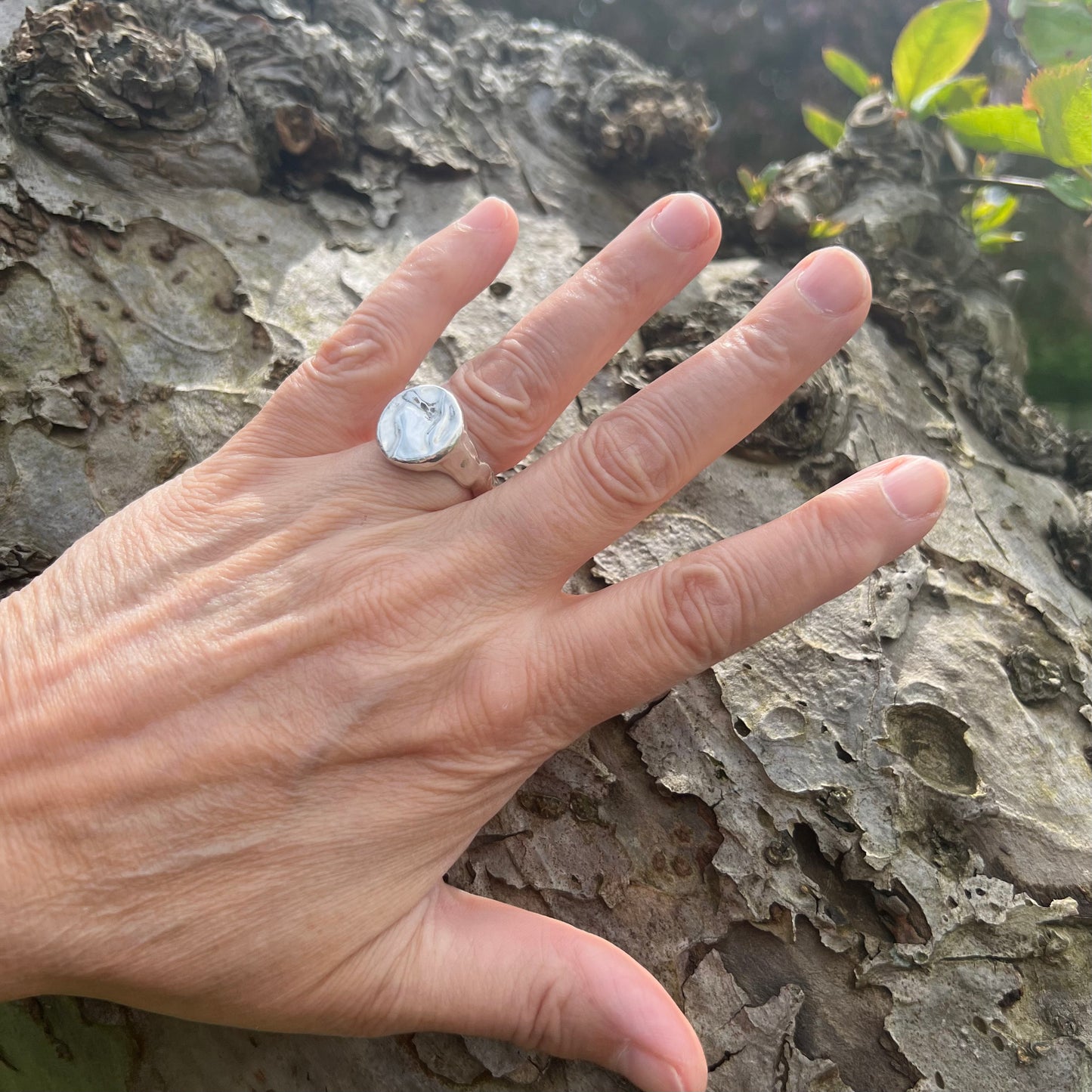 A shiny sterling silver splash ring on a hand with a tree in the background.