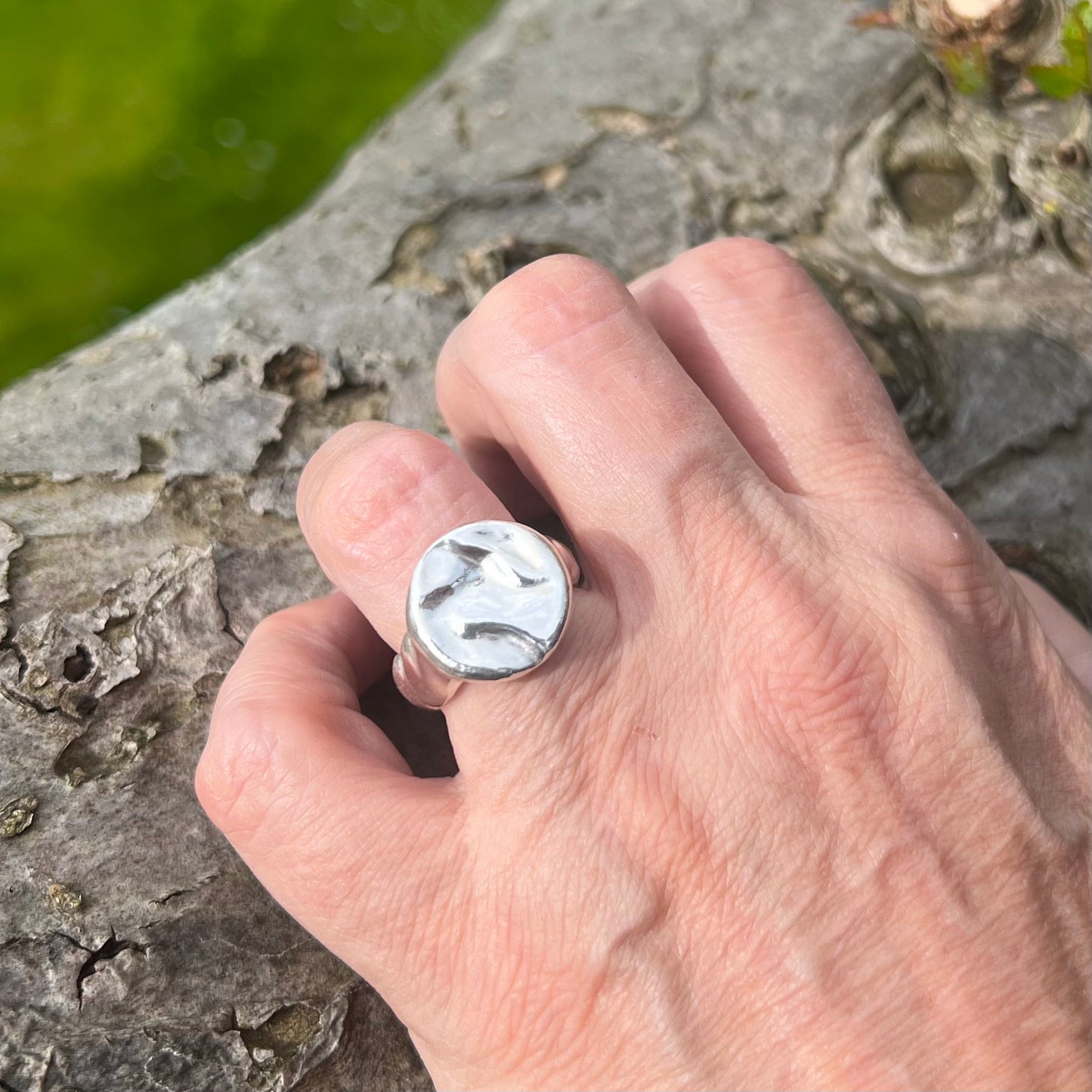 A matt sterling silver splash ring on a hand with a tree in the background.