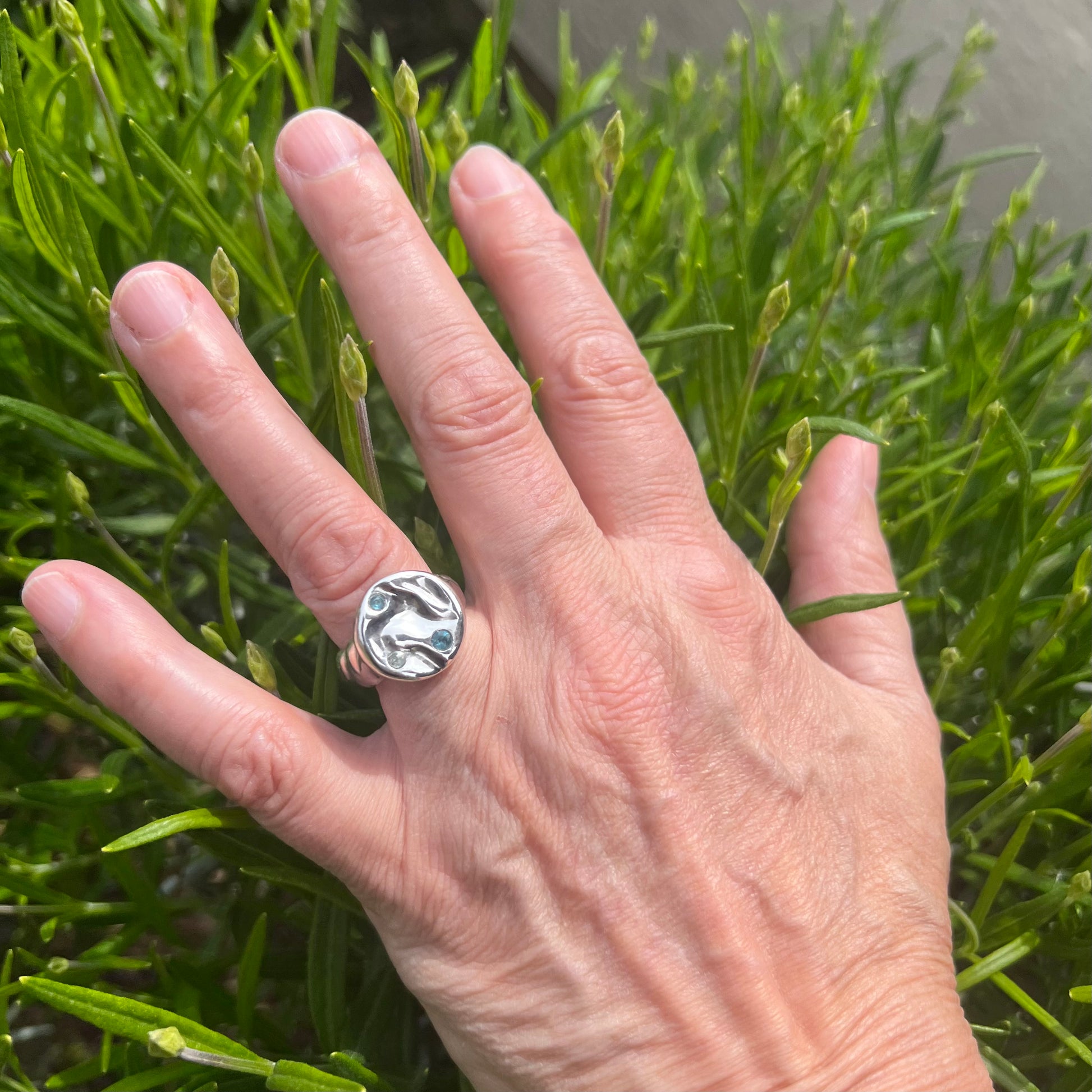 A triple topaz sterling silver splash ring on a hand with a shrub in the background.
