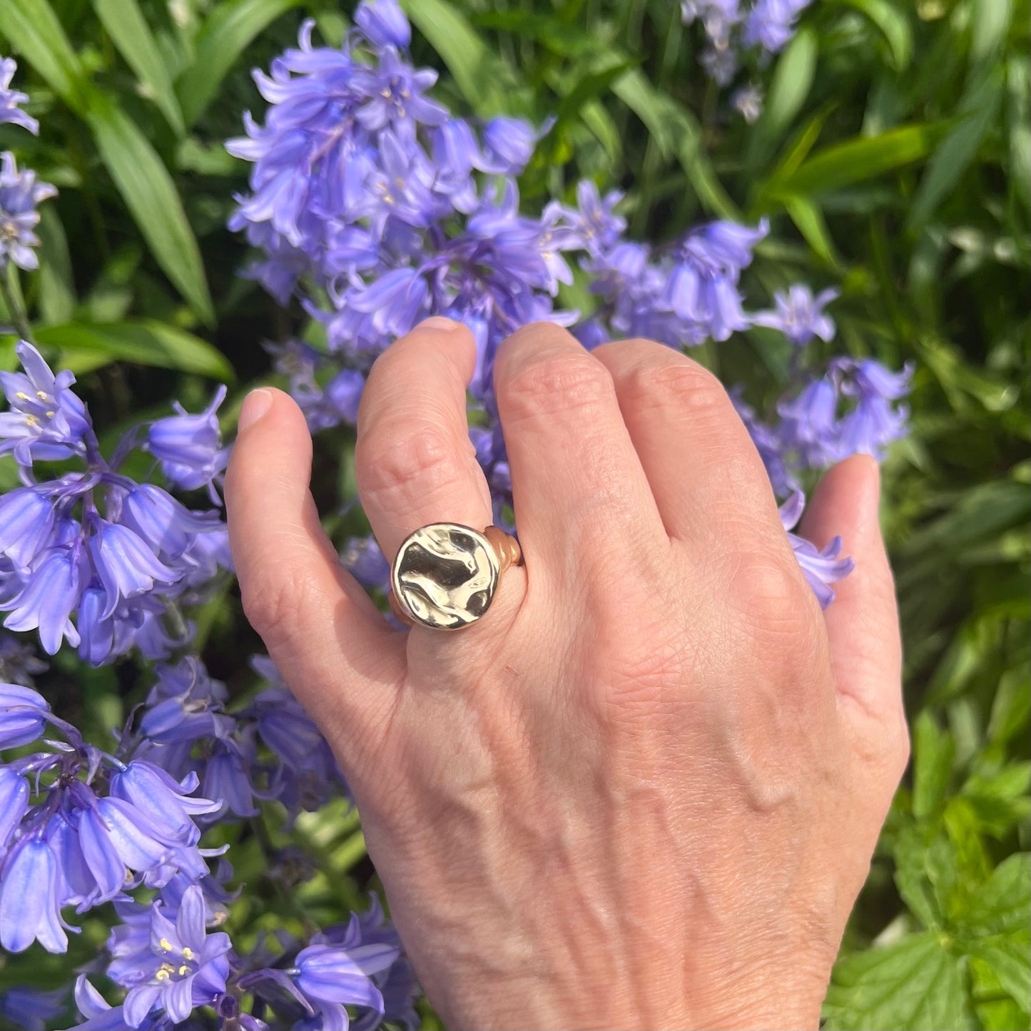 A solid 9ct yellow gold splash ring on a hand with a bluebell in the background.