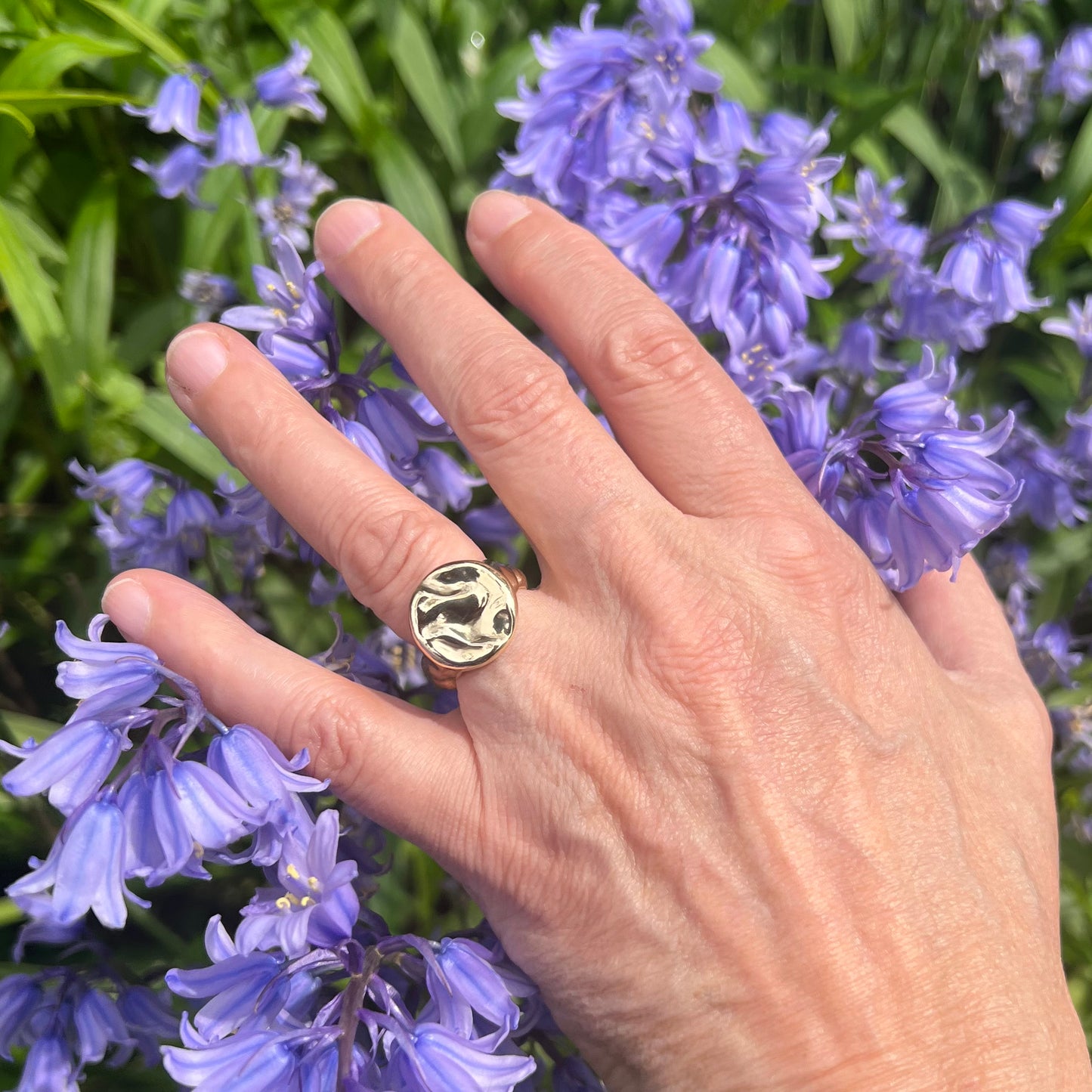 A solid 9ct yellow gold splash ring on a hand with a bluebell in the background.