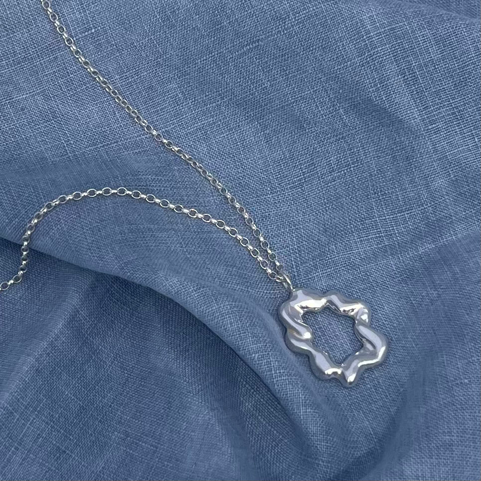 The 'Cloud pendant'. A handmade, sterling silver abstract shaped pendant. The background is blue linen.