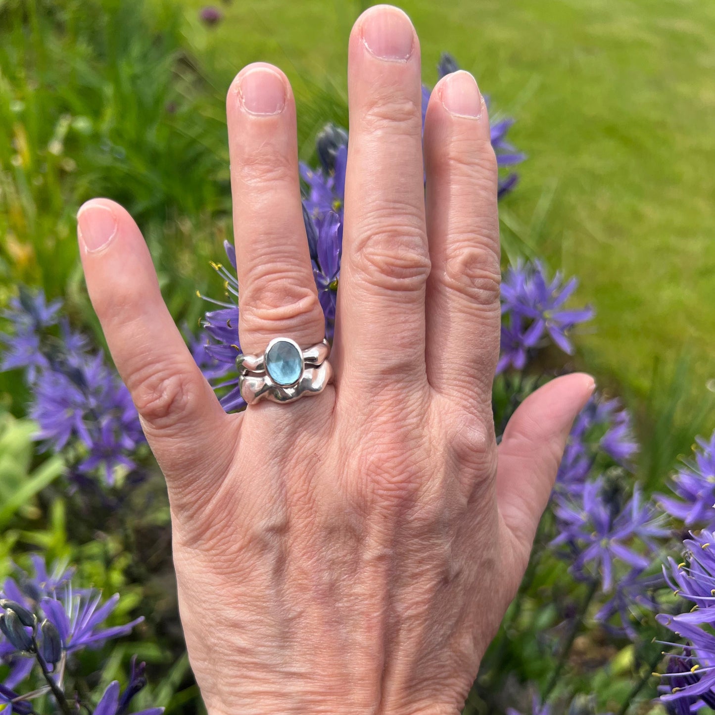 A sterling silver wave ring and a topaz set bubble ring on a background of purple flowers and grass