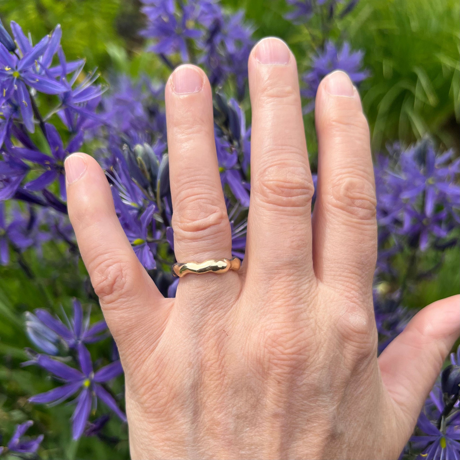 The gold bubble ring on a hand with purple flowers in the background.