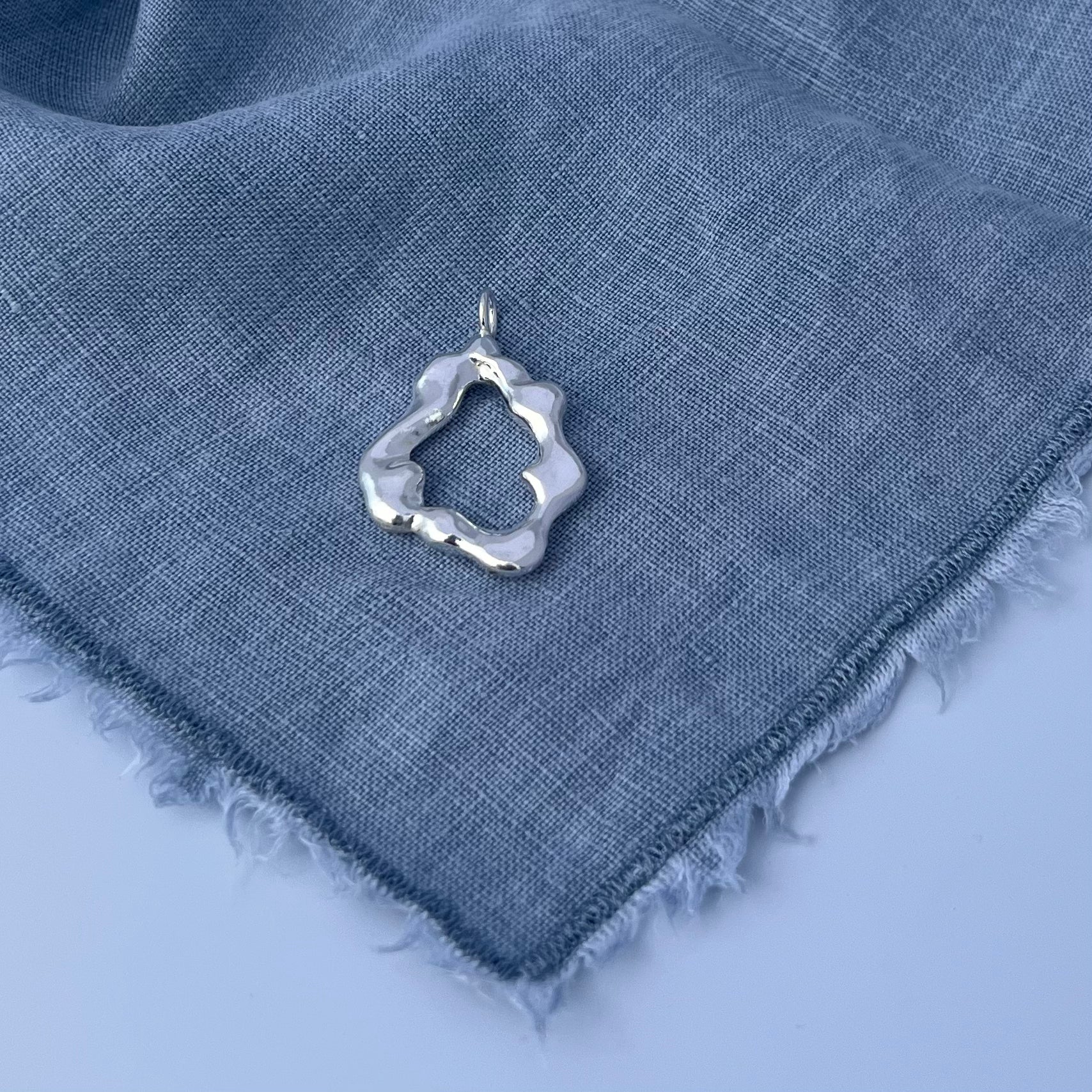 The 'Mist pendant'. A sterling silver abstract pendant. The background is blue linen.