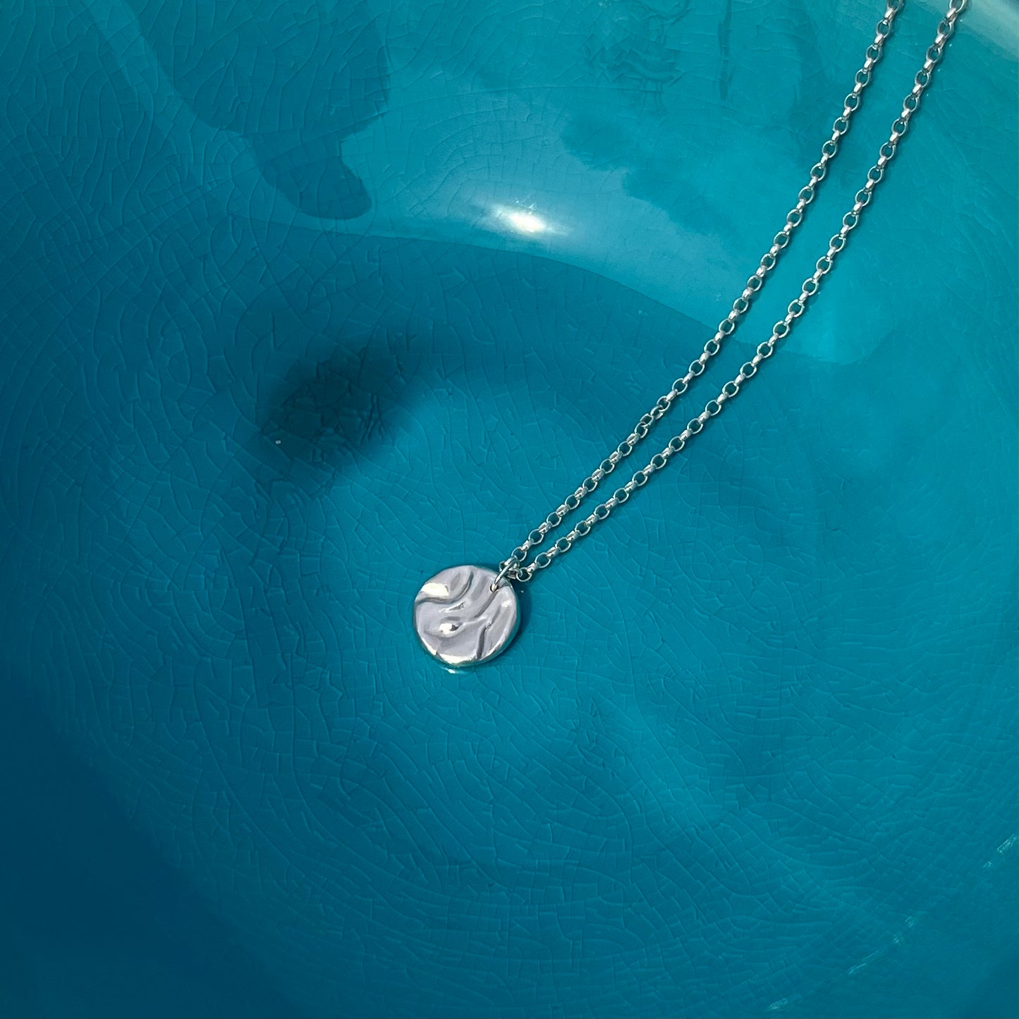 A sterling silver rock pool pendant and chain on an azure background.
