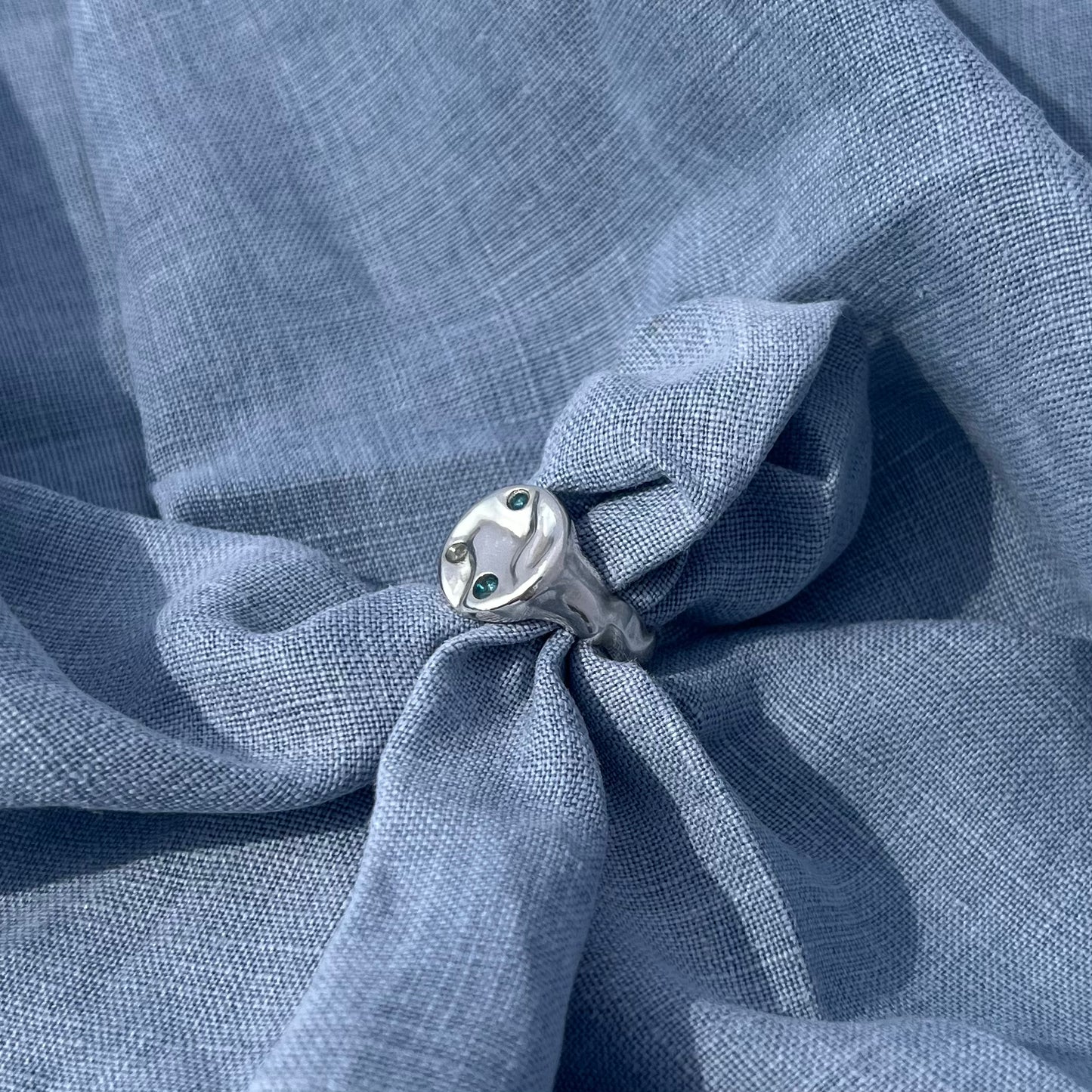A triple topaz sterling silver splash ring on a background of blue linen.  