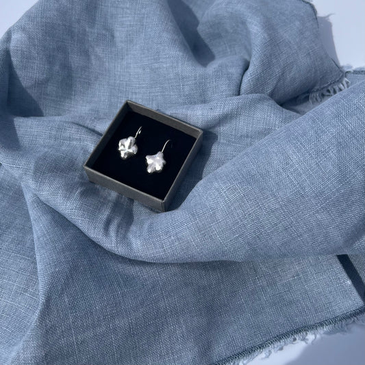 The swirl drop earrings in a black box, on a blue linen background.