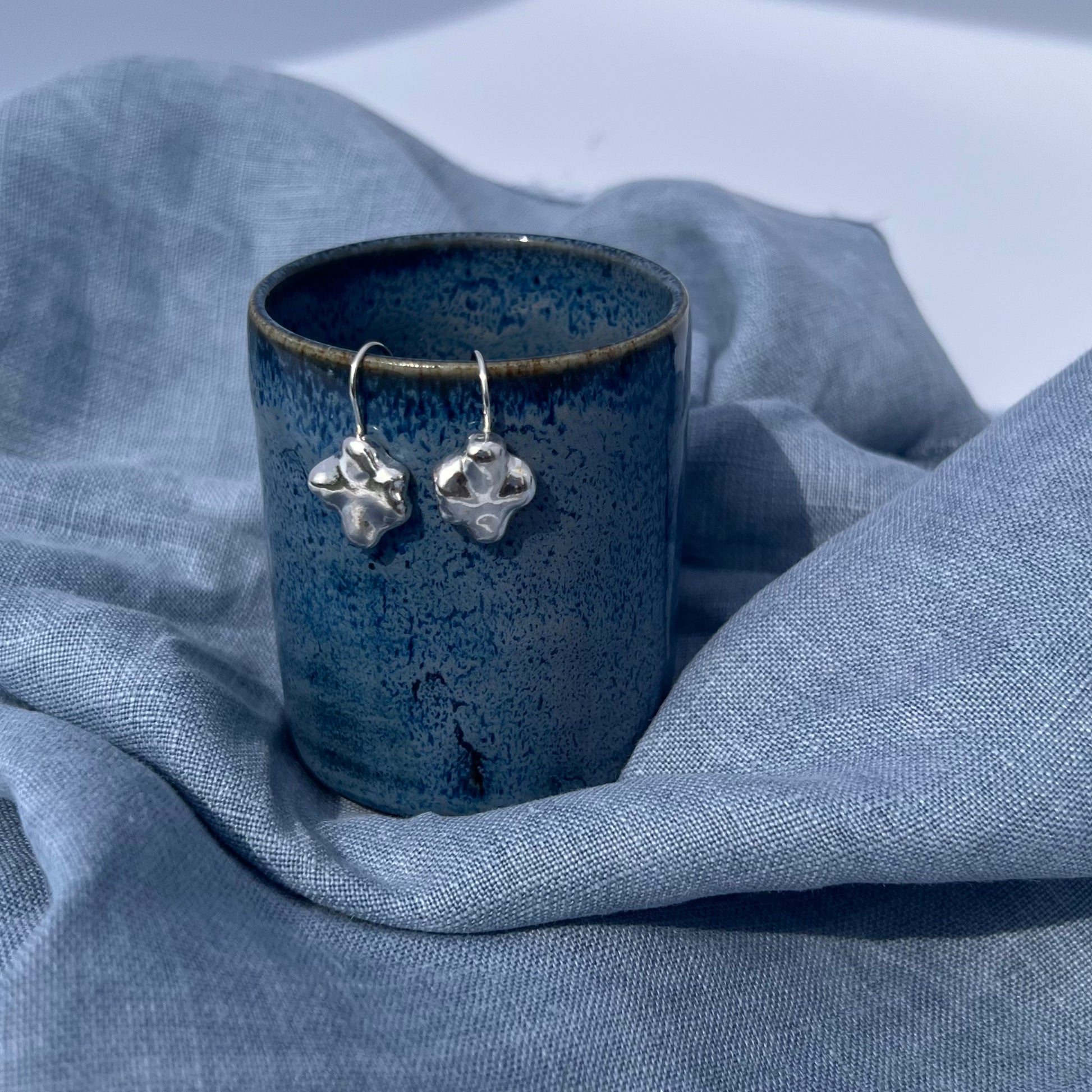 A pair of the sterling silver swirl drops hanging on a blue pot with a blue linen background.