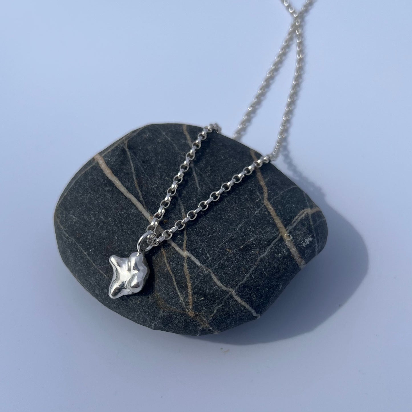 The swell pendant in sterling silver on a chain sitting on a rock with a white background.