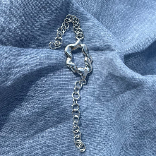 A chunky, statement handmade sterling silver bracelet on a blue linen background. The centrepiece of the bracelet is shaped like a cloud and it has a handmade hook clasp.