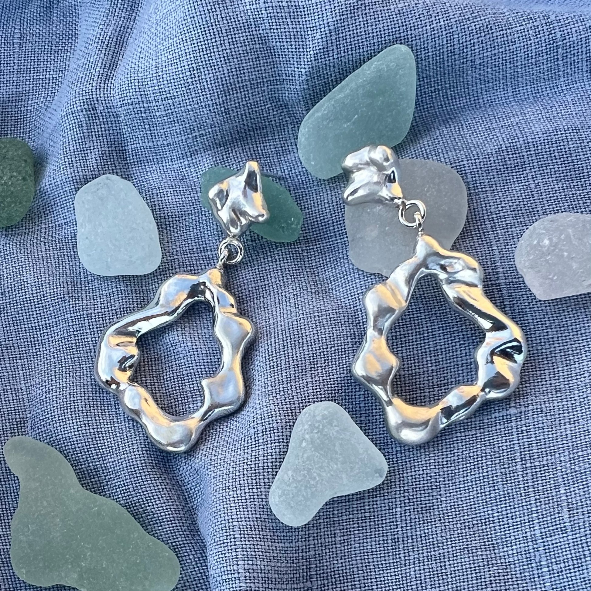 Chunky statement drop earrings on a background of blue linen and sea-glass. These earrings are handmade from recycled sterling silver and feature a stud, 2 linking hoops and then an abstract shape silver shape. 