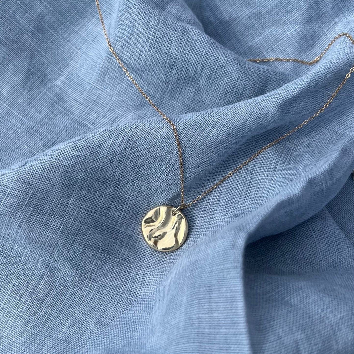 A handmade 'Rock-pool pendant" in recycled 9ct yellow gold. The pendant is on a chain and the background is of blue linen.