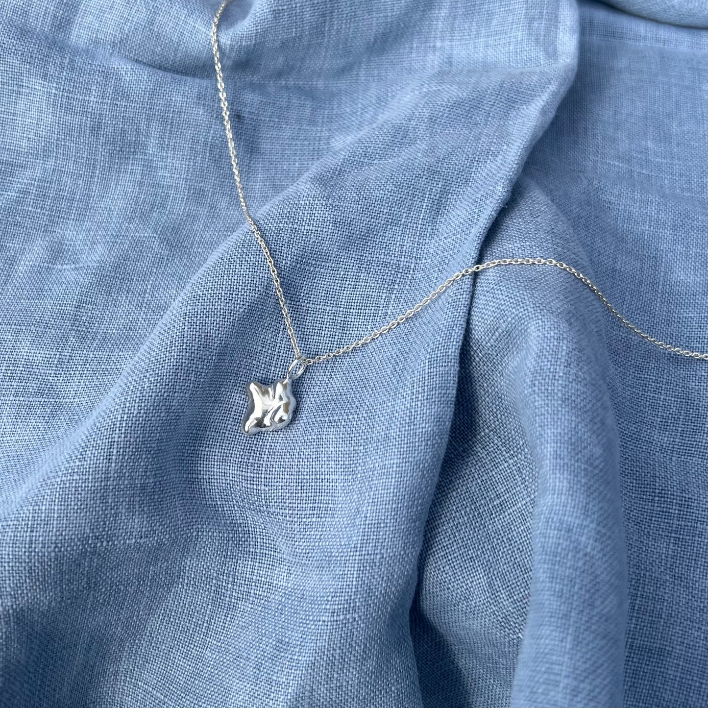 The swell pendant in sterling silver on a chain with a blue linen background.