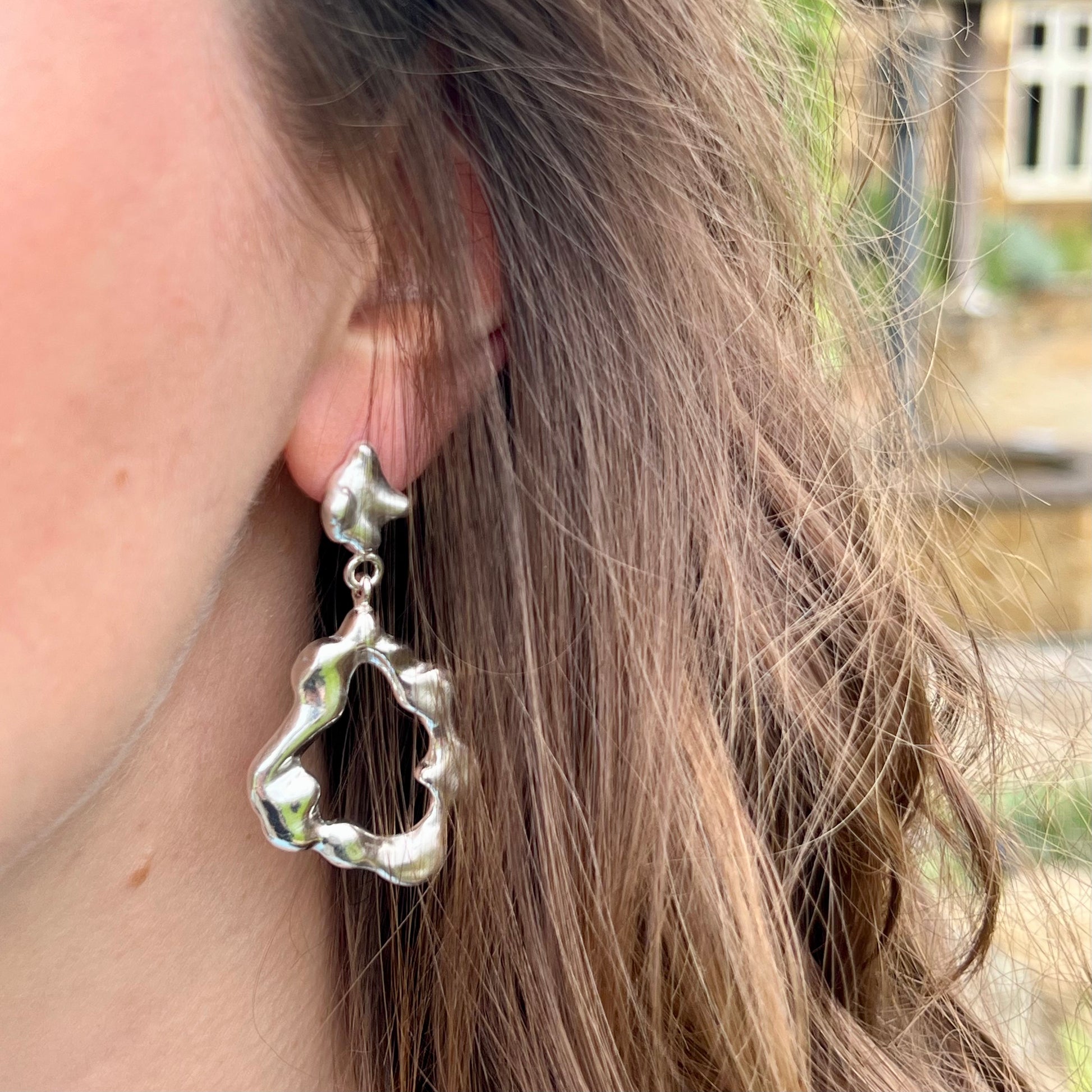 The right earring of the 'Drift earrings' photographed on a woman with long brown hair.