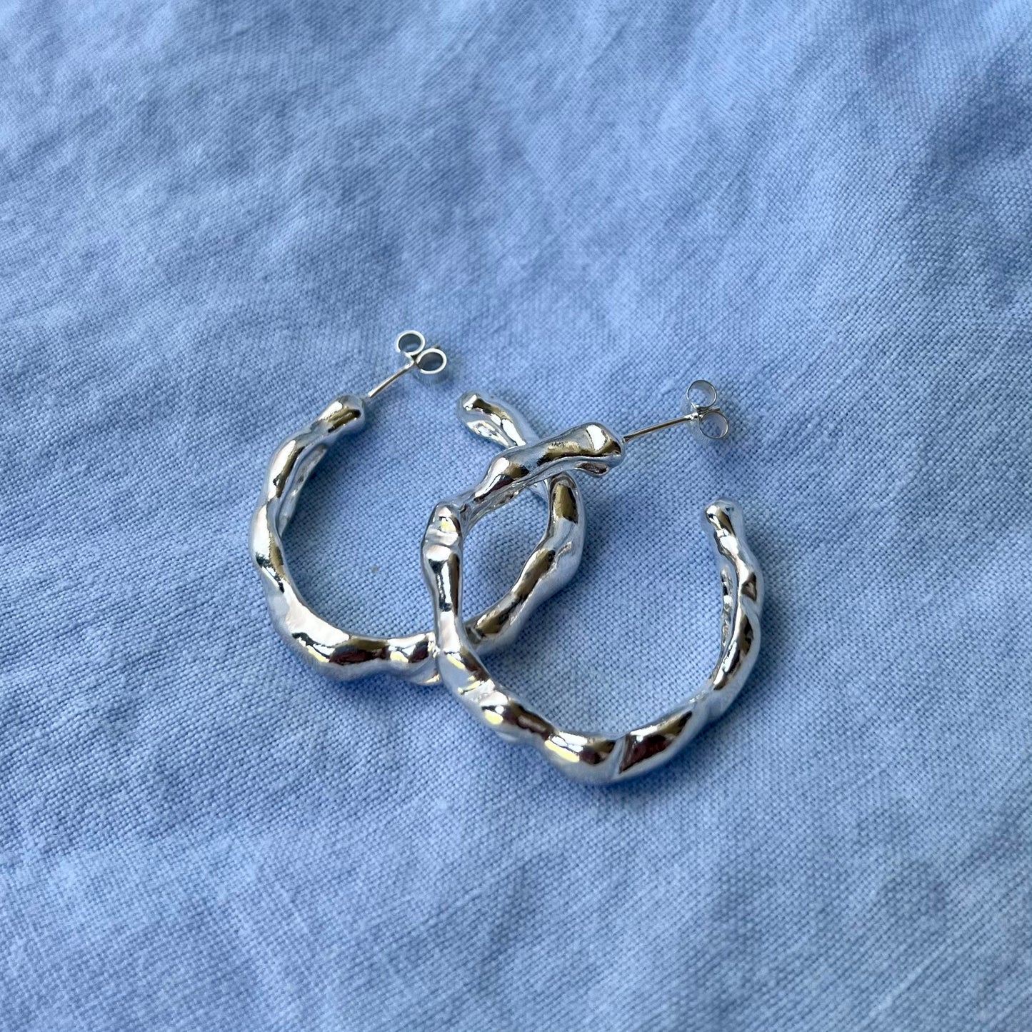 Large wavy sterling silver hoops on a blue linen background.