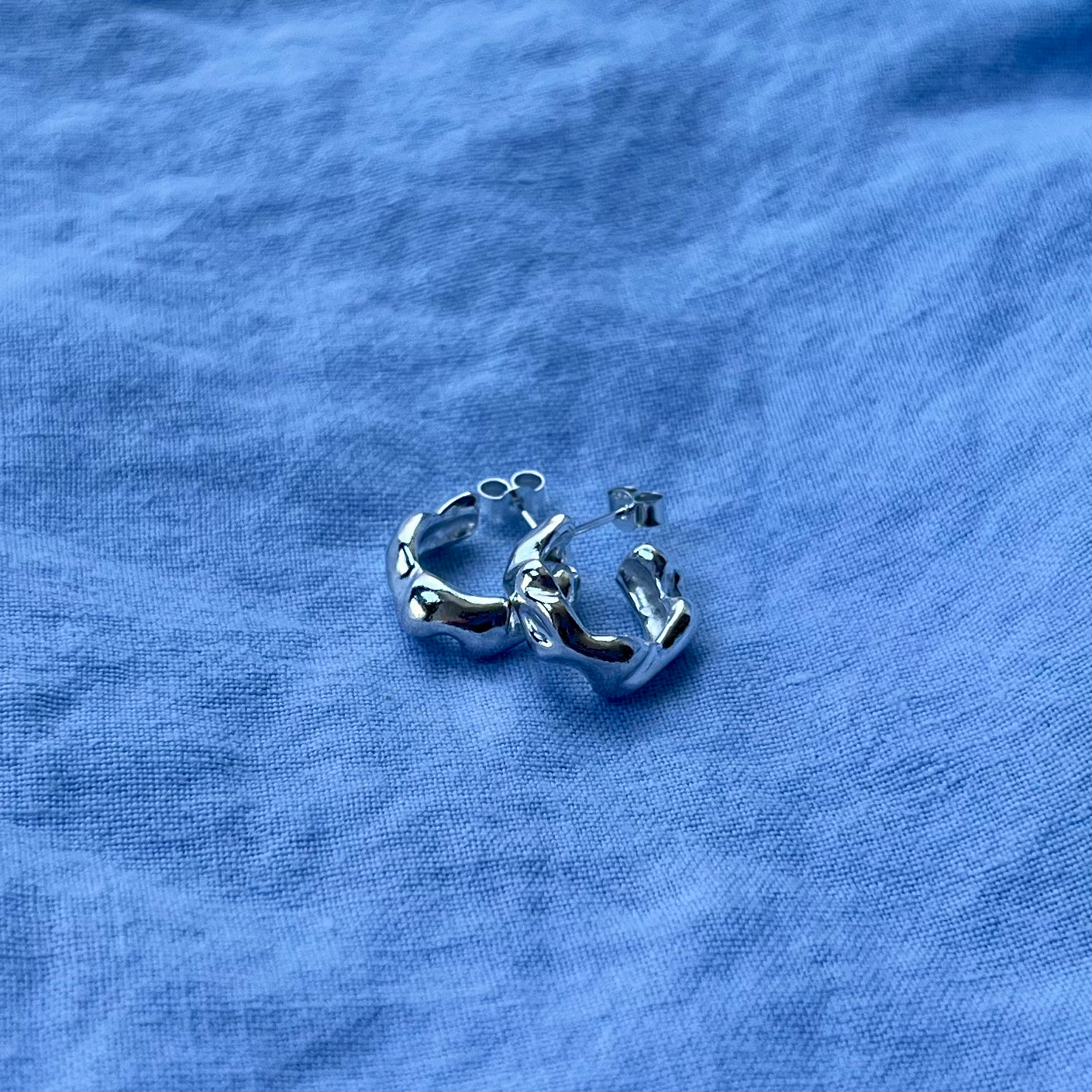 Small wavy silver earrings on a blue background.