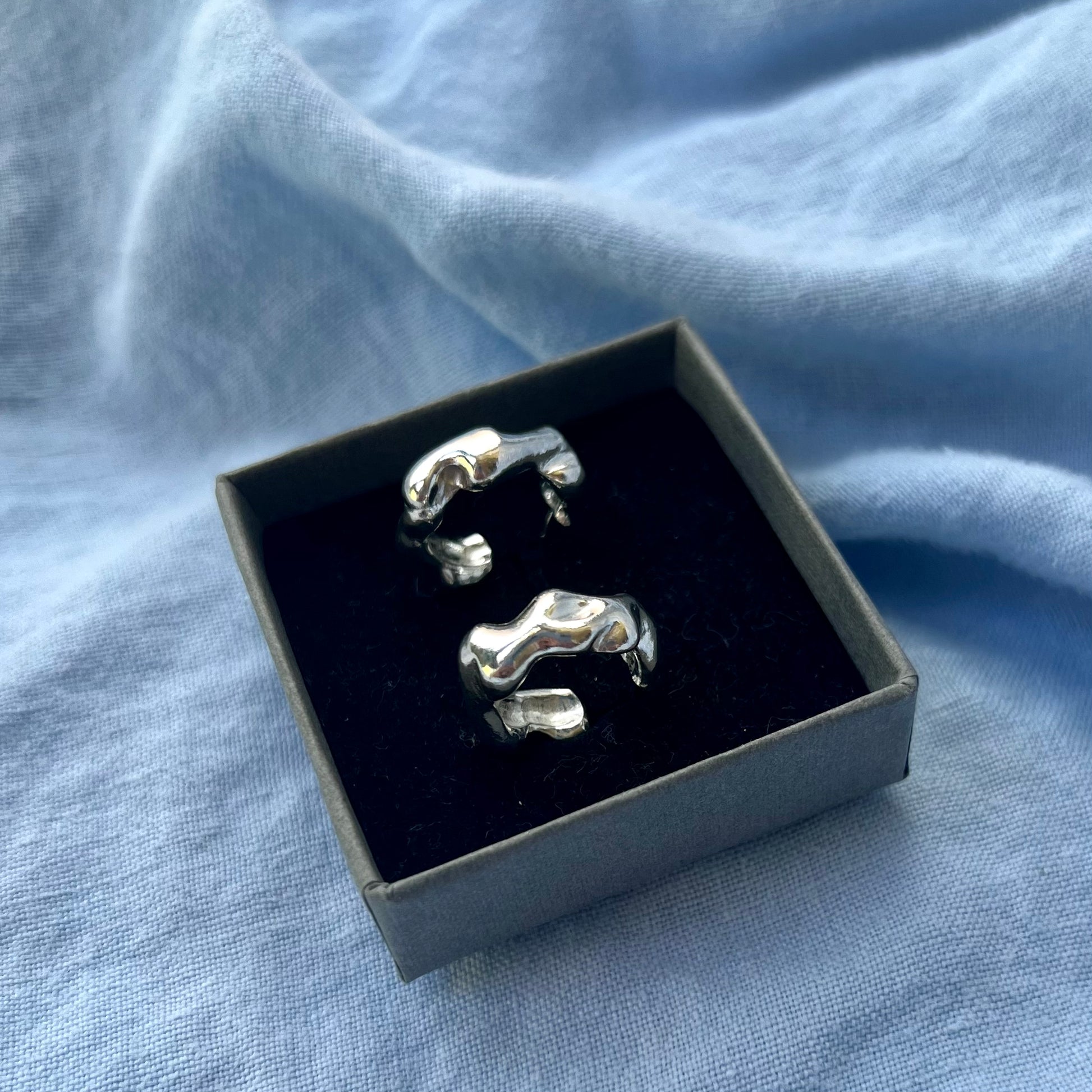 Small wavy silver earrings in a grey box on a blue background.