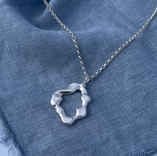 The 'Mist pendant'. A handmade, sterling silver abstract shaped pendant. The background is blue linen.