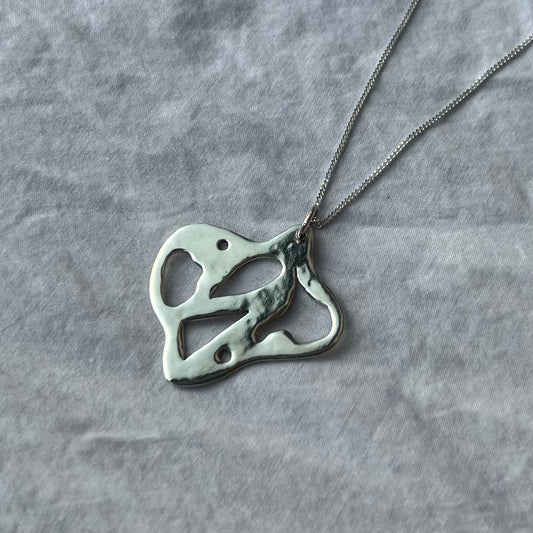 A handmade sterling silver charm in an abstract lemon shape with unique cut-outs. Pictured with a chain.
