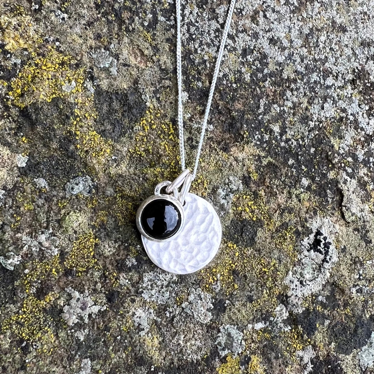 A onyx stone set in silver and a silver disc charmon a sterling silver chain.
