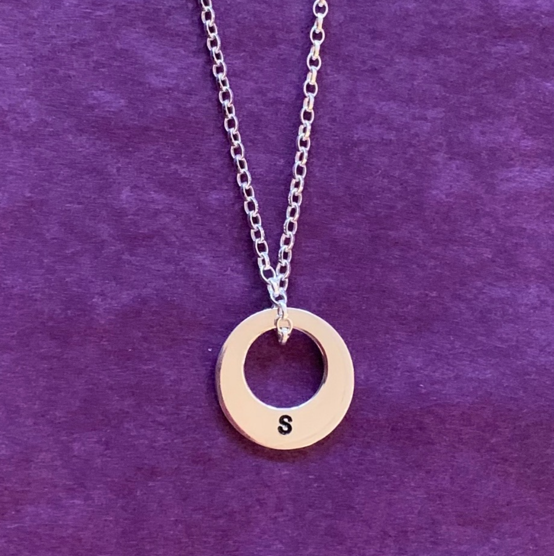 A sterling silver circular disc stamped with an S initial and on a silver chain.