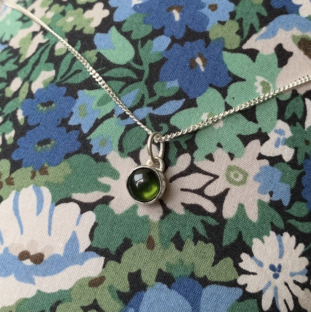 A green tourmaline set in silver forming a charm which is hung on a sterling silver trace chain.