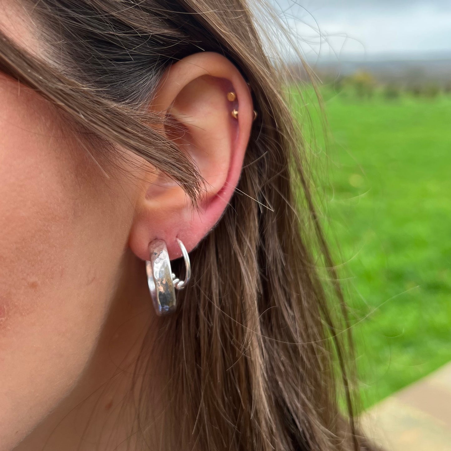Handmade sterling silver chunky hammered hoops earrings, pictured on a model.
