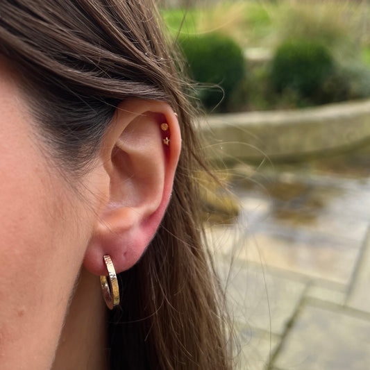 Handmade, solid 9ct gold hoop earrings with a lined hammer texture, pictured on a model.
