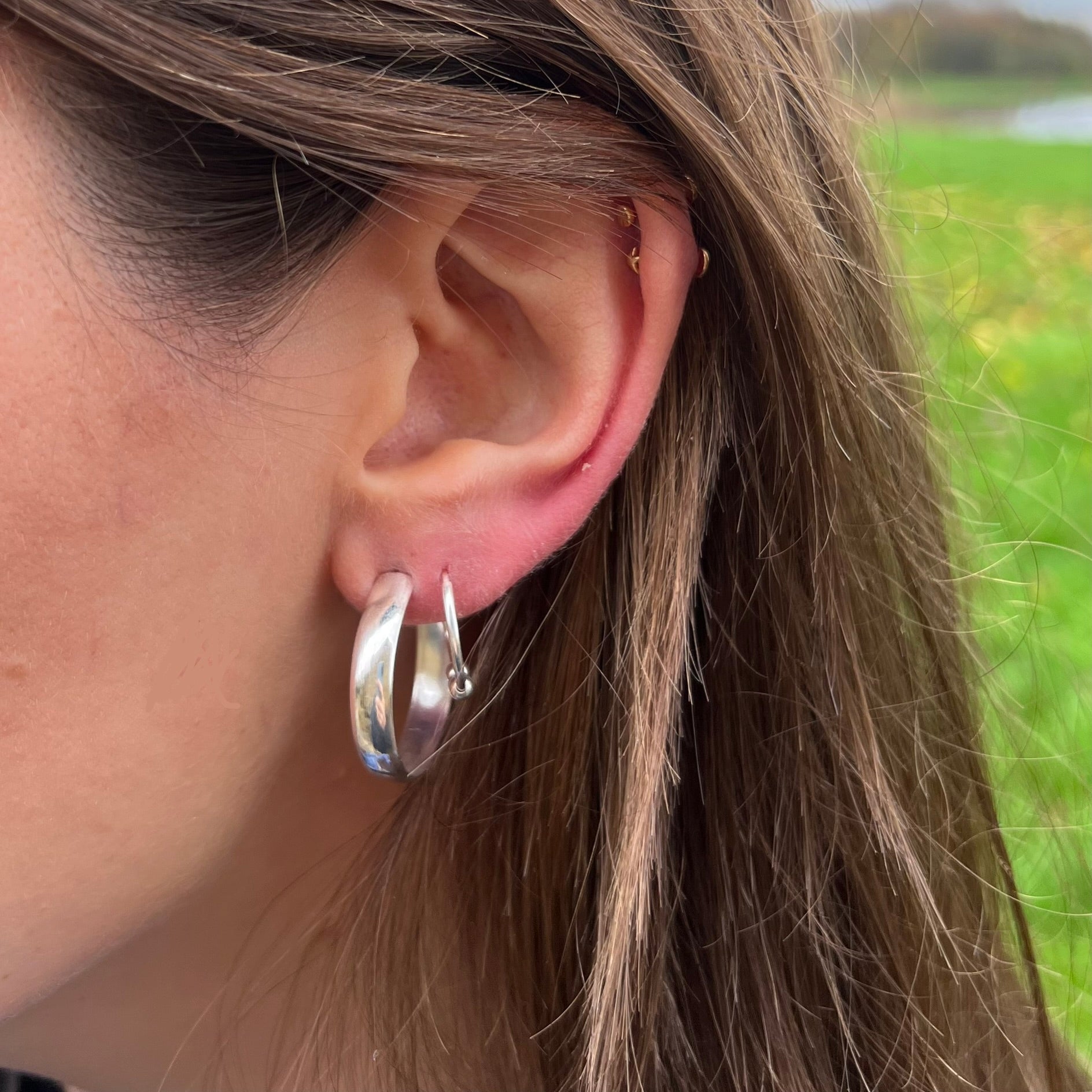 A pair of shiny sterling silver hoop earrings pictured on a models ear.