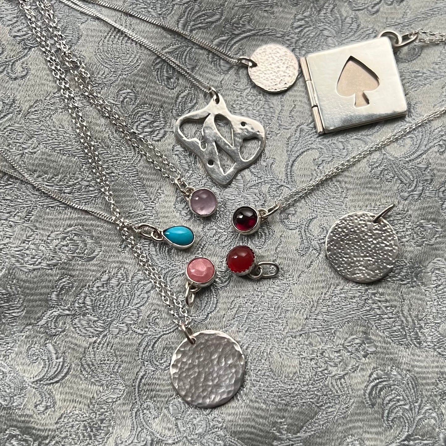 This picture shows a variety of sterling silver pendants including several bezel set gemstone charms.